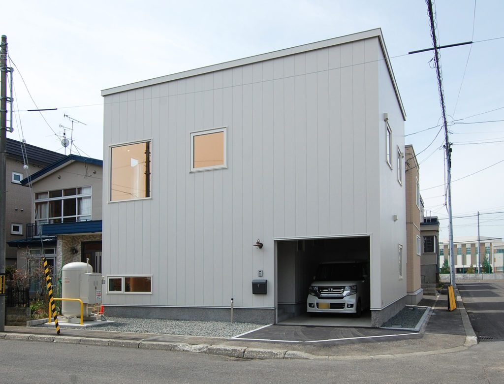 アイボリーの金属サイディングとビルトインガレージを採用したシンプルモダンな住宅の外観」
