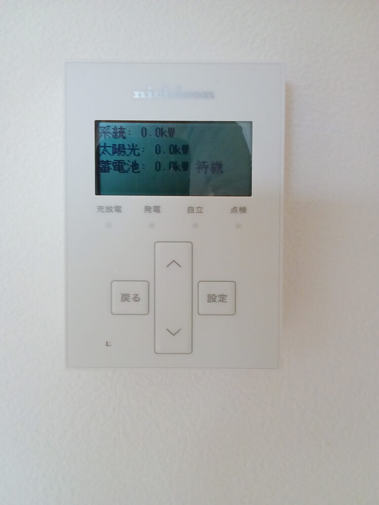 太陽光、蓄電池の稼働状態が0.0kWの待機状態として表示されている、壁掛けされたニチコン（nichicon）製リモコンモニター