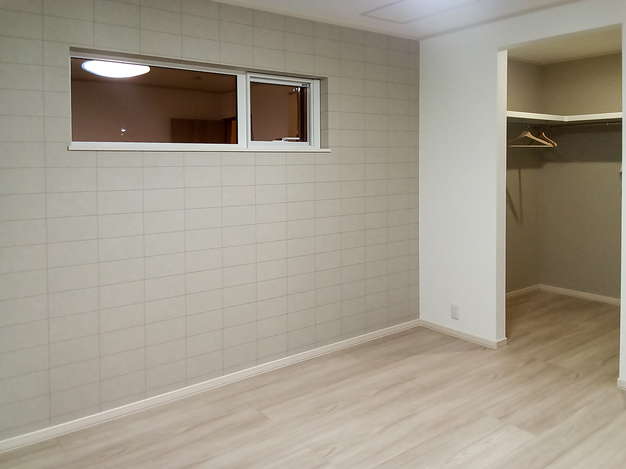 主寝室の夜の様子。ダウンライトや間接照明で壁のタイル調アクセントクロスが浮かび上がり、落ち着いた雰囲気を演出している。